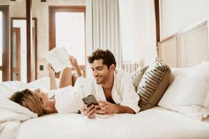 梅里达CIGNO HOTEL BOUTIQUE- Adults Only的男人和女人躺在床上看手机