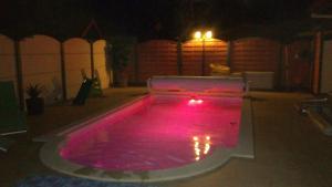 拉特斯特德布赫LA MAISON DES HIPPOCAMPES的夜间后院的游泳池,有粉红色的灯光