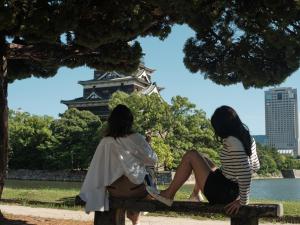 广岛FAV HOTEL HIROSHIMA STADIUM的两个女人坐在塔楼前的长凳上
