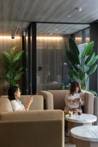 函馆FAV HOTEL HAKODATE的坐在一个房间看手机的两名妇女