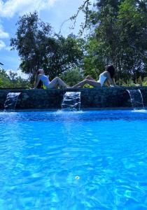 哈伯勒内Habarana Tree House Ambasewana Resort的两个女人躺在游泳池旁边的墙上