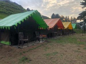 KheergangaCity Escape Camps and Cafe Kheerganga的田野里一排带椅子的帐篷