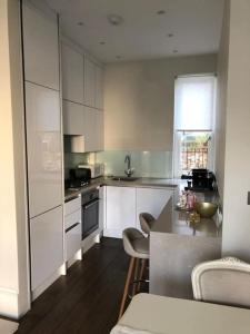 伦敦Stylish 3-bedroom flat in Kensington的厨房配有白色橱柜和桌椅