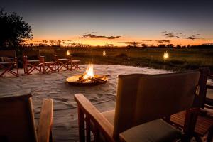 Okavango DeltaAmber River Camp的露台上的火坑,配有椅子,享有日落美景