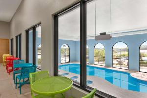 布兰森AmericInn by Wyndham Branson & Conference Center的一个带五颜六色椅子和桌子的游泳池,位于带窗户的房间内