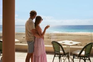 莫罗德哈布雷Iberostar Selection Fuerteventura Palace的一对夫妇站在窗户前,享有海滩美景