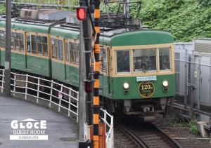 镰仓市GLOCE 鎌倉 若宮大路House お部屋から江ノ電ビューを独り占め 鎌倉駅から徒歩3分的轨道上的绿色和黄色火车