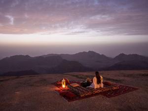 瓦迪穆萨Grand Mercure Petra的坐在山间帐篷旁边的毯子上的女人