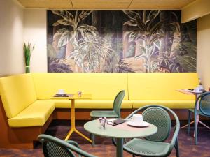 佩皮尼昂佩皮尼昂中心美居酒店的餐厅里一张黄色的沙发,配有桌椅