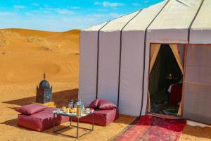 姆哈米德Erg Chegaga Camp Excursions的沙漠中的帐篷,前面有桌子