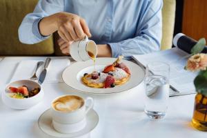 苏黎世Park Hyatt Zurich – City Center Luxury的坐在桌子上的人,拿着一盘煎饼和咖啡