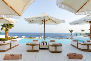 沙姆沙伊赫Meraki Resort Sharm El Sheikh Adults only的一个带游泳池、椅子和遮阳伞的度假村