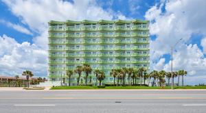 加尔维斯敦Galveston Luxury High Rise Oceanfront的一座绿色的大建筑,前面有棕榈树