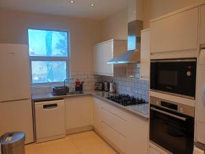 伦敦London Luxury Spacious 2 Bedroom Apartment 4 mins from Ilford Stn. FREE parking的厨房配有白色橱柜和窗户。