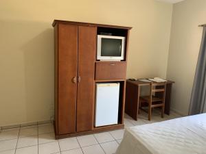 欧里尼奥斯Ouro Hotel的一间带电视和小冰箱的橱柜的卧室