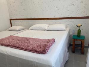 普拉杜Casa de praia Prado Ba Doces magnólias的一张带两个枕头的床和一张带花瓶的桌子