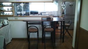 大分ゲストハウス小富士的厨房配有带凳子的桌子和冰箱。