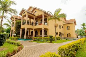 吉塞尼Elevate Suites Gisenyi的棕榈树和车道的大型黄色房屋