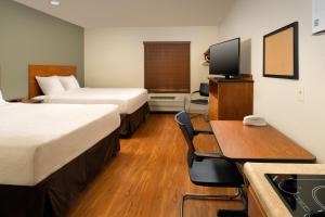 戴维Extended Stay America Select Suites - Fort Lauderdale - Airport - West的酒店客房设有两张床、一张桌子和一台电视。