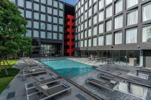 芭堤雅市中心Best Western Plus Nexen Pattaya的大楼前带躺椅的酒店游泳池