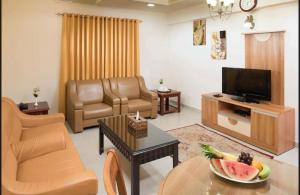 马斯喀特AL MANAF HOTEL SUITES的客厅配有电视和一张带一碗水果的桌子