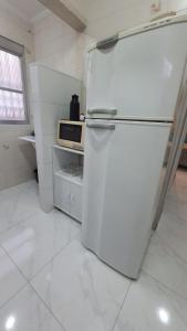 大普拉亚113 SOL & MAR I com VARANDA - 1 dormitório - Canto do FORTE - 300 m da Praia e 20m da Avenida dos Barzinhos - ESTACIONAMENTO gratuito e WI Fi 300mbytes com TV a cabo - ap113的白色的厨房配有冰箱和微波炉。