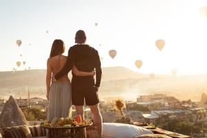 格雷梅Doors Of Cappadocia Special Cave Hotel的男人和女人站在阳台上,看着热气球