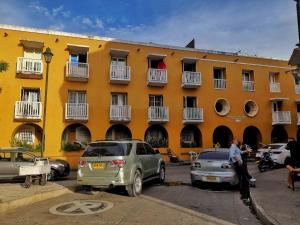 卡塔赫纳Happy tours apartments的一座黄色的建筑,汽车停在停车场