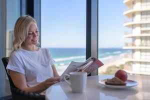 黄金海岸Meriton Suites Surfers Paradise的坐在桌子旁读书的女人