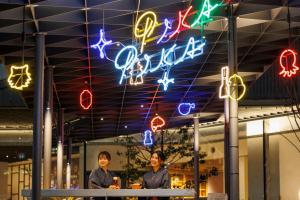 大阪OMO7 Osaka by Hoshino Resorts的两个妇女站在一间商店前面,有 ⁇ 虹灯标志