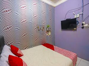 名古屋OYO 91782 Satria Homestay Syariah的一间卧室配有一张带红色枕头的床和一台电视。