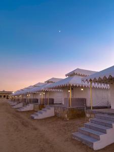 斋沙默尔Best Desert Camp In Jaisalmer Red Velvet的黄昏时沙漠中的一排帐篷