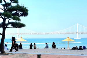 釜山JJ House Gwangan Beach的一群人,在海滩上行走,在后面有一座桥