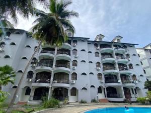 瓜埠阿迪亚纳公寓的一座白色的大建筑,前面有一棵棕榈树