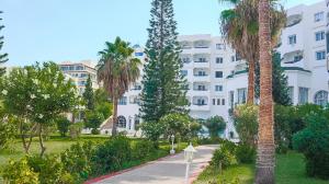 苏塞Hotel Royal Jinene Sousse的一座白色的大建筑,种植了棕榈树,设有人行道