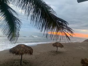 翡翠海岸Mar De Estrellas - Hotel的海滩上的两把草伞和大海