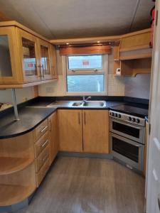 锡德卡普Quite 3 Bedroom Static Caravan的厨房配有木制橱柜、水槽和炉灶。