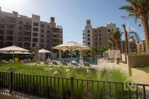 迪拜Veluxa - Luxury and bright 1 bedroom apartment, Burj view!的一个带遮阳伞和桌椅的游泳池以及大楼
