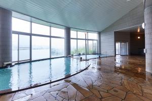 一关KAMENOI HOTEL Ichinoseki的一座大型室内游泳池,位于一座带窗户的建筑中