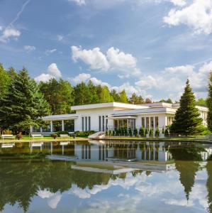 纳达金Perła Leśna Nadarzyn的一座白色的建筑,前面有一个池塘
