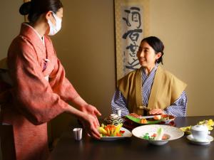 山之内町玉露祖亚日式旅馆的戴面具的女人,为餐桌上的女人提供食物