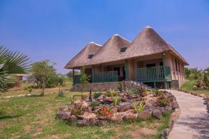 AruaTilenga Safari Lodge的茅草屋顶和花床的房子