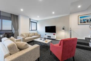 悉尼Meriton Suites Kent Street, Sydney的客厅配有沙发、椅子和电视