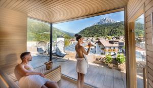 费拉迪普利米罗Brunet - The Dolomites Resort的一对夫妇站在房子的阳台上,眺望着群山