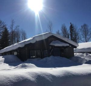 OckelboStugaNäraKungsberget - mysig stuga med kamin, grillkåta och vedbastu的雪覆盖的房子,后面有太阳