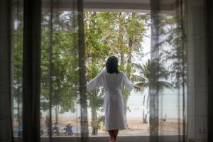 芭东海滩Anona Beachfront Phuket Resort-SHA EXTRA PLUS的穿着白色衣服的女人从窗口望出去