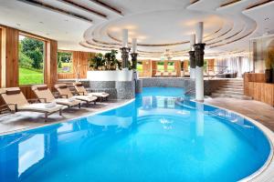 埃尔毛伊尔玛因提洛尔运动酒店的酒店大堂的大型蓝色泳池,配有椅子