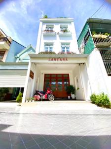 大叻Lantana Homestay的一座白色的建筑,前面停有一辆摩托车