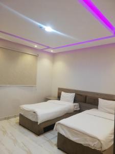 达瓦迪米المغتره للشقق الفندقيه的天花板上紫色灯的客房内的两张床