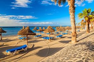 阿罗纳Rosamar 211 Los Cristianos Ocean Views的一个带草伞和椅子的海滩和大海